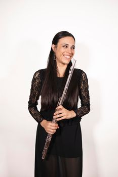 A young elegant female flutist smiling and looking to the side while holding her instrument