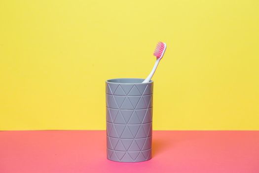 A pink toothbrush is standing in a gray glass. Dental care concept