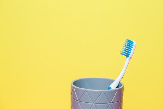 A blue toothbrush is standing in a gray glass. Dental care concept