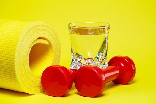 red dumbbells, a glass of water, a yellow rug, colored background, sports, energy drink, equipment for the gym