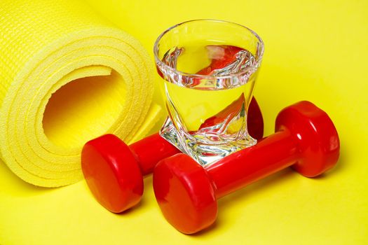 red dumbbells, a glass of water, a yellow rug, colored background, sports, energy drink, equipment for the gym