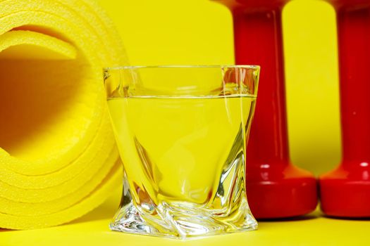 red dumbbells, a glass of water, a yellow rug, colored background, sports, energy drink, equipment for the gym