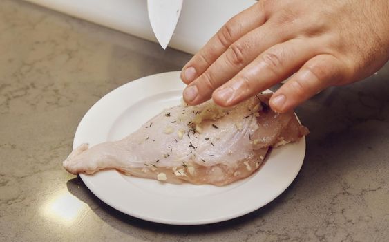 The cook sprinkled the chicken breast with salt. The hands of the cook rub the meat with spices.