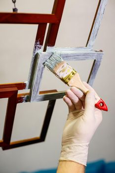 the master paints with a brush a wooden brown photo frame with light paint