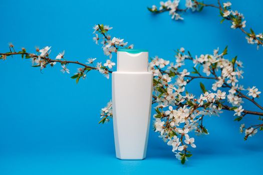 white bottle with cream, shampoo for hair, shower gel, isolated blue background, beauty and youth of the human body, flowering tree