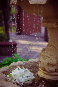 The Wedding Bouquet Of The Bride Of Red Roses Lies In An Old Fountain Under Splashes And Drops Of Water.. bridal bouquet of flowers in fountain water drops