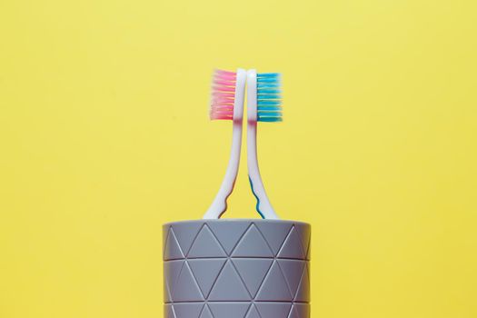 Two toothbrushes stand with a gray glass on a yellow background. Toothbrush concept for a couple, living together as the beginning of a family