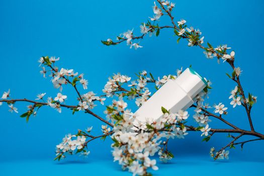 white bottle with cream, shampoo for hair, shower gel, isolated blue background, beauty and youth of the human body, flowering tree