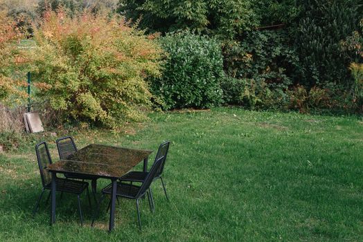 Metal garden bistro table and chair. The coffee bar restaurant empty white wooden tables and brown chairs in the sun on grass and dirt took on a sunny summer day. Wooden seat in a city park. Picnic in the park. Rest in the open area.