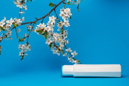 white bottle with cream, shampoo for hair, shower gel, isolated blue background, beauty and youth of the human body, flowering tree