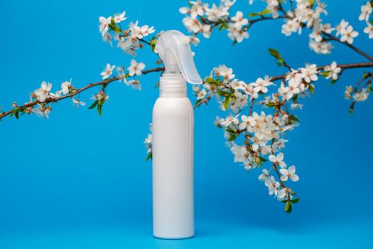 white bottle with cream, shampoo for hair, shower gel, isolated blue background, beauty and youth of the human body, flowering tree
