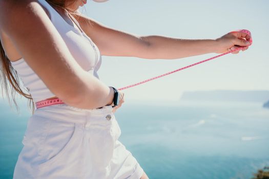 a young and slender woman in shorts holds in her hand a measuring yellow tape on her sexy thighs on the beach. concept of detox and diet