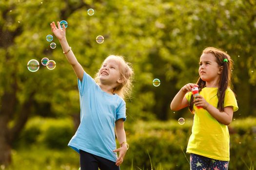 Two little girls are blowing soap bubbles, outdoor shoot