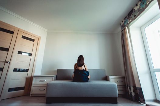 Loneliness. Alienation. Girl in an empty room sits back on a couch and stares in the wall