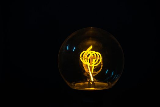 A classic Edison light bulb on black background with space for text. Illuminated light bulb on black background.