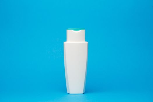 white bottle with cream, hair shampoo, shower gel, isolated blue background, human body beauty