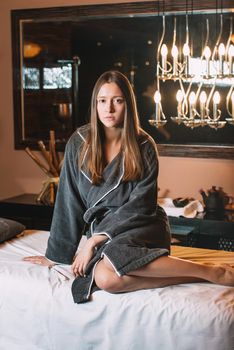 Young charming girl in a gray bathrobe waiting for procedure. beautiful woman spending time at modern spa cabinet for relaxing. Soft yellow light