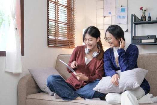 Happy asian female friends at home sitting on couch. two young women with chatting on sofa gossiping and sharing secrets discussing life and relations. Friendship trust concept.