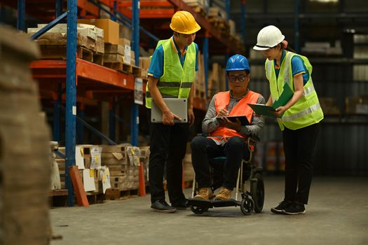 Male manager in wheelchair and workers working together in warehouse. Manufacture storehouse occupation concept.