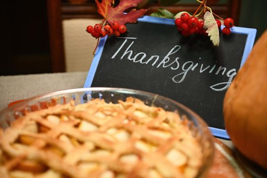 Selective focus. Branch of viburnum berries hanging on a chalkboard with lettering Thanksgiving Day, red autumn maple leaves, a sweet homemade classic American pumpkin apple pie with crispy crust