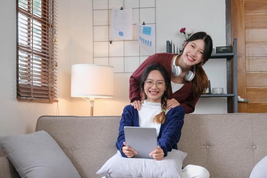 Happy asian female friends at home sitting on couch. two young women with chatting on sofa gossiping and sharing secrets discussing life and relations. Friendship trust concept.