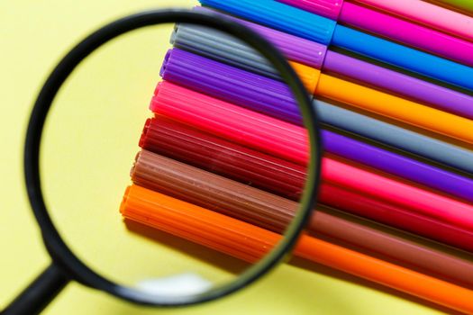 multi-colored markers for drawing through a magnifying glass on a yellow background
