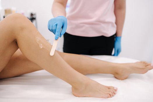 Woman beautician in blue glowes applies contact gel on the leg of a woman for laser hair removal in medical clinic. Close up.