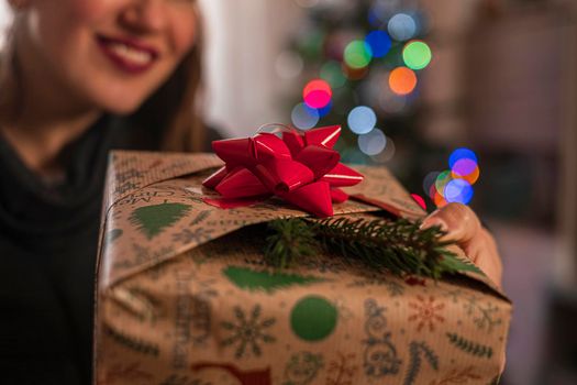 Happy woman holds a decorative gift in her hands. Close up.Blurred Christmas tree on background. Christmas card with space for text .