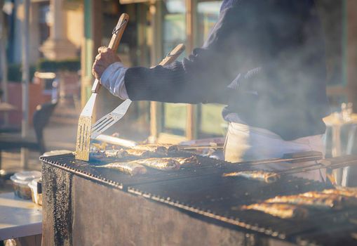 Man cooks herring on the grill on a street market