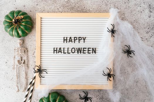 Happy halloween holiday concept. Skeletons, spider, web, pumpkin, text on board frame on concrete grey background. Halloween festival, greeting card