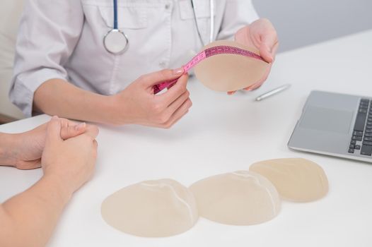 A plastic surgeon measures breast implants with a centimeter tape and demonstrates to a female patient