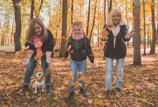 Grandmother and mother with granddaughter throw up fall leaves in autumn park and having fun. Generation, leisure and family concept