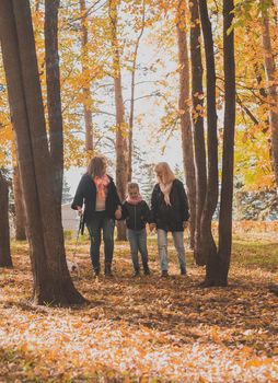 Grandmother and mother with granddaughter throw up fall leaves in autumn park and having fun. Generation, leisure and family concept