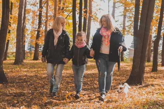 Grandmother and mother with granddaughter throw up fall leaves in autumn park and having fun. Generation, leisure and family concept