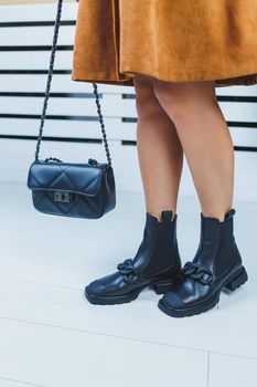 Close-up of female legs in black leather lace-up shoes. Black leather handbag in female hands. New autumn collection of women's leather shoes 2022