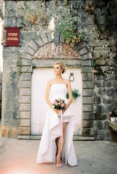 Bride in a white dress with a cutout stands near an ancient stone building. High quality photo
