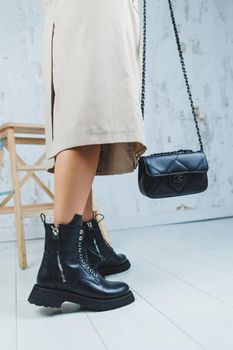 Close-up of female legs in black leather lace-up shoes. Black leather handbag in female hands. New autumn collection of women's leather shoes 2022