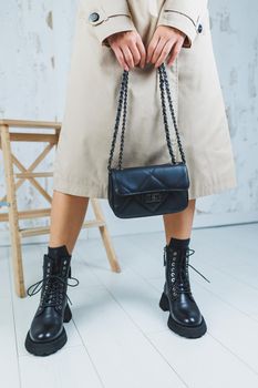 Close-up of female legs in black leather lace-up shoes. Black leather handbag in female hands. New autumn collection of women's leather shoes 2022