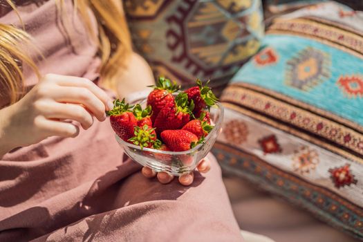 Portrait of gorgeous woman wearing beautiful dress sitting in a patio and eating strawberry.