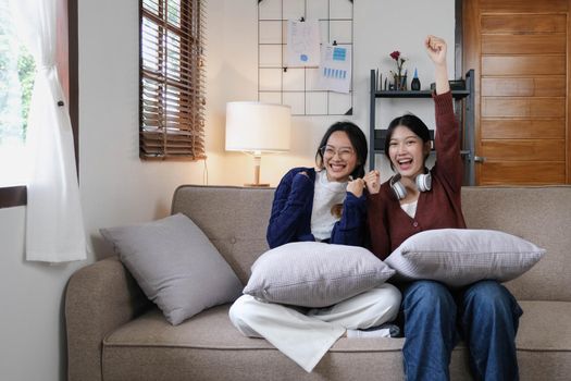 Two Young woman cheering together for sport on TV in cozy living room at home..