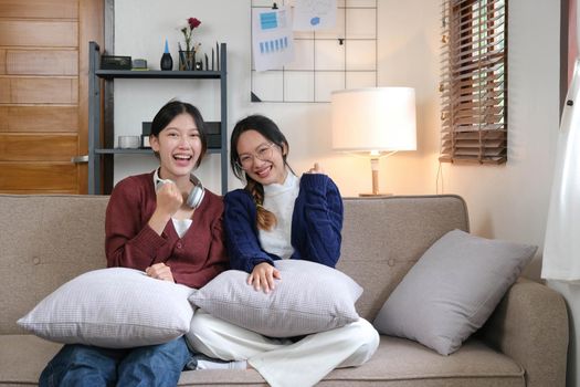 Two Young woman cheering together for sport on TV in cozy living room at home..