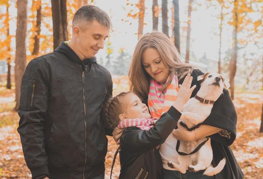 Family spend time in autumn park with a dog. Father, mother and daughter and jack russell terrier dog having fun in fall.