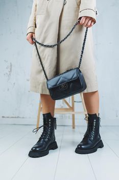 Close-up of female legs in black leather lace-up shoes. Black leather handbag in female hands. New autumn collection of women's leather shoes 2022