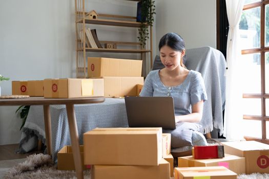 Start up small business, SME female owner checking order online to prepare to pack a box of goods for sale to customers, sme business idea