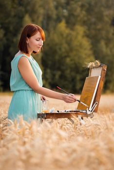 Red-headed female artist working in nature on warm summer evening time, vertical photo