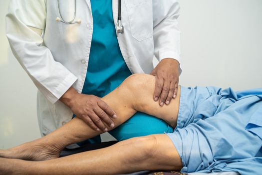 Asian doctor physiotherapist examining, massaging and treatment knee and leg of senior patient in orthopedist medical clinic nurse hospital.