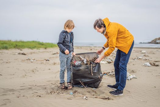 Dad and son in gloves cleaning up the beach pick up plastic bags that pollute sea. Natural education of children. Problem of spilled rubbish trash garbage on the beach sand caused by man-made.