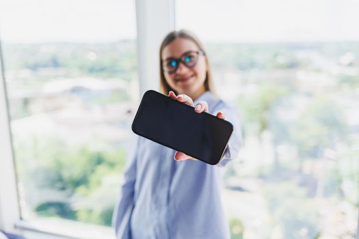 A modern mobile phone with a black screen is held in the hands of a woman, female hands with a smartphone close-up