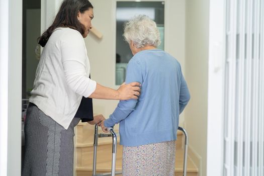 Caregiver help asian or elderly old woman walk with walker support up the stairs in home.
