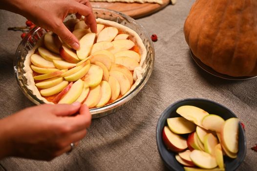 Close-up. Hands of a woman housewife or chef confectioner, putting slices of apple in circle on top of pumpkin pie. Preparing traditional American classic festive pie for Thanksgiving Day. Halloween